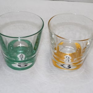 May include: Two clear glass tumblers with a green and yellow band around the middle. The green tumbler has the number "6" in white on the band. The yellow tumbler has the number "8" in white on the band.