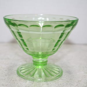 May include: A green glass footed bowl with a fluted design. The bowl is clear and has a textured surface.