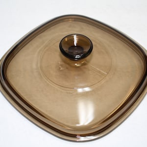 May include: A square, brown glass lid with a knob on top. The lid is designed for a square baking dish.