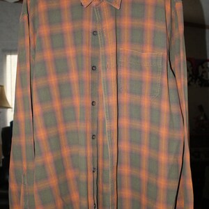 May include: A long-sleeved plaid shirt in shades of orange and green. The shirt has a button-down collar and a chest pocket. The label on the shirt reads "Ridgecut Indonesia".