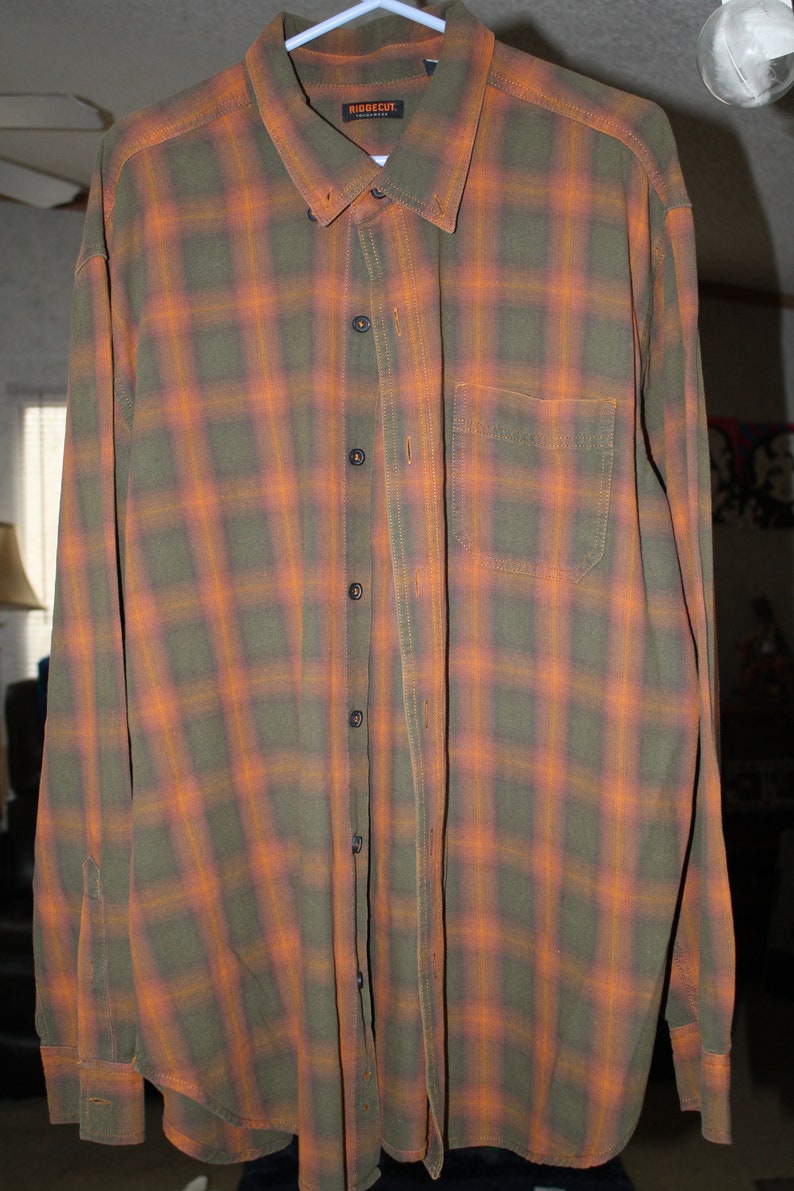 May include: A long-sleeved plaid shirt in shades of orange and green. The shirt has a button-down collar and a chest pocket. The label on the shirt reads "Ridgecut Indonesia".