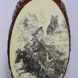 May include: Oval wooden plaque with a bark edge, featuring a black and white illustration of Native American riders on horseback, a bear, and a mountain scene. The artwork is printed on a cream-colored background.