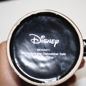 Puede incluir: Taza de cer&aacute;mica negra con un logotipo de Disney blanco y el texto "Microwave and Dishwasher Safe Made in China".