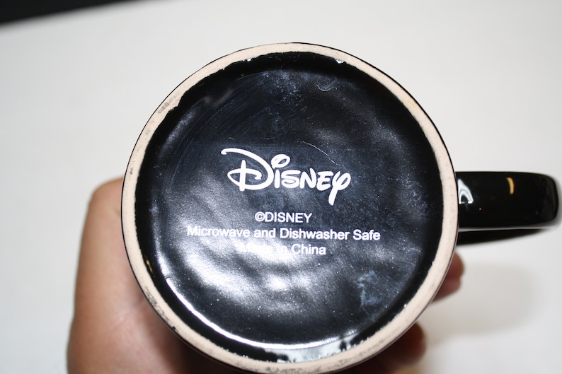 Puede incluir: Taza de cer&aacute;mica negra con un logotipo de Disney blanco y el texto "Microwave and Dishwasher Safe Made in China".