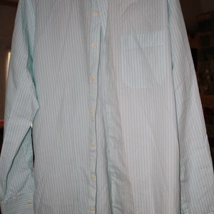 May include: A light blue and white striped long-sleeve dress shirt with a button-down collar and a single chest pocket. The shirt has a Peter Millar brand label.