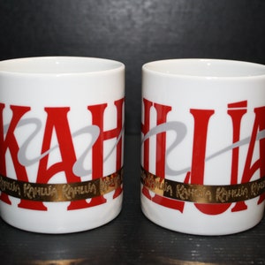 May include: Two white ceramic mugs with red and gray lettering that reads "KAHLUA" with a gold band around the bottom of each mug that reads "KAHLUA KAHLUA KAHLUA".