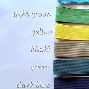Peut inclure: Un assortiment de bandes &eacute;lastiques de diff&eacute;rentes couleurs et motifs, notamment blanc, rouge &agrave; pois, bleu ciel &agrave; pois, vert clair, jaune, kaki, vert, bleu fonc&eacute;, noir et rose fonc&eacute;. Les bandes &eacute;lastiques sont dispos&eacute;es verticalement sur une surface blanche.