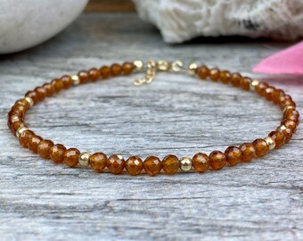May include: A delicate gold chain bracelet with small, faceted, amber-colored beads.