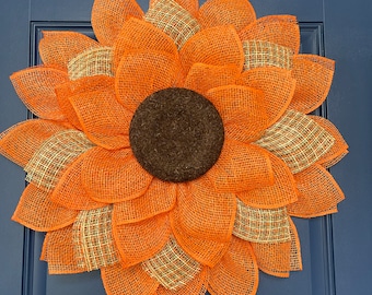 May include: A large orange and brown burlap sunflower wreath with a brown center. The wreath is hanging on a blue door.
