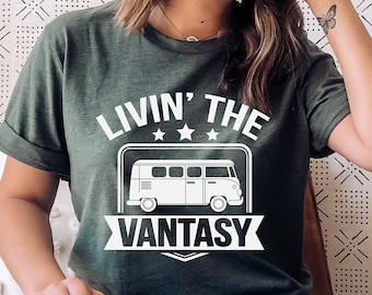 May include: A dark olive green short-sleeve t-shirt featuring a white graphic of a vintage van. The text above the van reads "LIVIN' THE" with three stars, and the text below the van reads "VANTASY" inside a banner design on the chest.