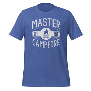 May include: A heathered blue short-sleeve t-shirt featuring a white distressed graphic print on the chest. The design includes a central campfire icon inside a circle, flanked by the text "MASTER" above and "OF THE CAMPFIRE" below.