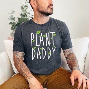 May include: A dark gray t-shirt with the text "PLANT DADDY" in white lettering and green leaf accents.