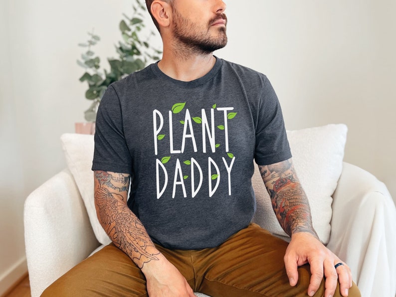 May include: A dark gray t-shirt with the text "PLANT DADDY" in white lettering and green leaf accents.