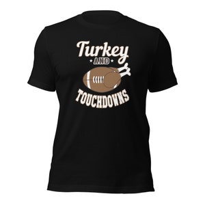 Op de afbeelding: Zwart T-shirt met een bruine kalkoen en voetbal afbeelding. De tekst "Turkey and Touchdowns" is op het shirt gedrukt.