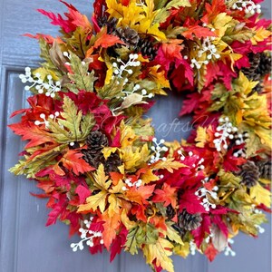 K&ouml;nnte beinhalten: Ein lebendiger Herbstkranz mit bunten Ahornbl&auml;ttern in Rot-, Orange- und Gelbt&ouml;nen. Der Kranz ist mit kleinen Tannenzapfen und wei&szlig;en Beerenzweigen geschm&uuml;ckt und schafft eine festliche saisonale Dekoration.