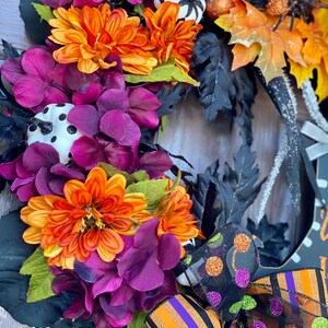 May include: A Halloween wreath with black, orange, and purple flowers, black leaves, and a black and white polka dot pumpkin. The wreath is decorated with a black and orange striped ribbon and a black mesh ribbon with green and orange polka dots.