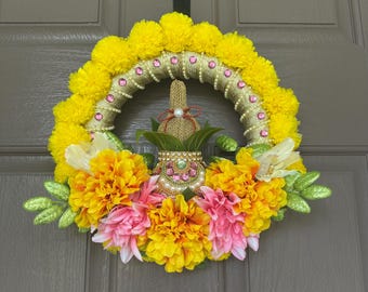 Puede incluir: Una vibrante corona decorativa con un diseño central con un arco dorado con cuentas adornado con gemas rosas y pompones amarillos brillantes. La corona está adornada con flores amarillas y rosas y hojas verdes brillantes.