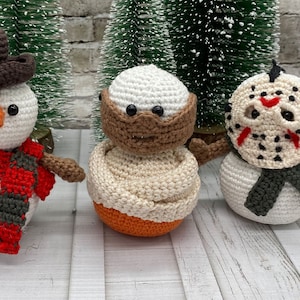 Peut inclure: Trois bonhommes de neige en crochet, chacun avec une personnalité différente. L'un porte un chapeau brun et une écharpe rouge et grise, l'autre a un masque facial brun et le troisième a un masque blanc avec des accents rouges et un couteau ensanglanté.