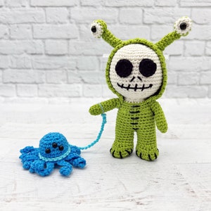 May include: A green crocheted skeleton wearing a green alien costume with large eyes and holding a blue crocheted octopus on a string.