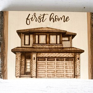 May include: A wood burned sign with the text "first home" and a drawing of a two-storey house with a garage.