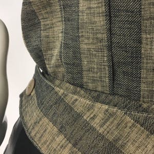 Puede incluir: Primer plano de una tela a rayas negras y beige con un detalle de bot&oacute;n. La tela tiene una textura tejida y un brillo sutil.