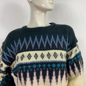 Pode incluir: Um su&eacute;ter de tric&ocirc; com padr&atilde;o creme, preto, roxo e azul.