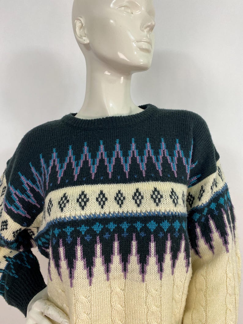 Pode incluir: Um su&eacute;ter de tric&ocirc; com padr&atilde;o creme, preto, roxo e azul.