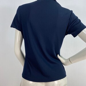 May include: Navy blue short-sleeved collared shirt. The shirt has a classic polo design with a button-up collar and a tailored fit. The fabric appears to be a smooth, solid color.