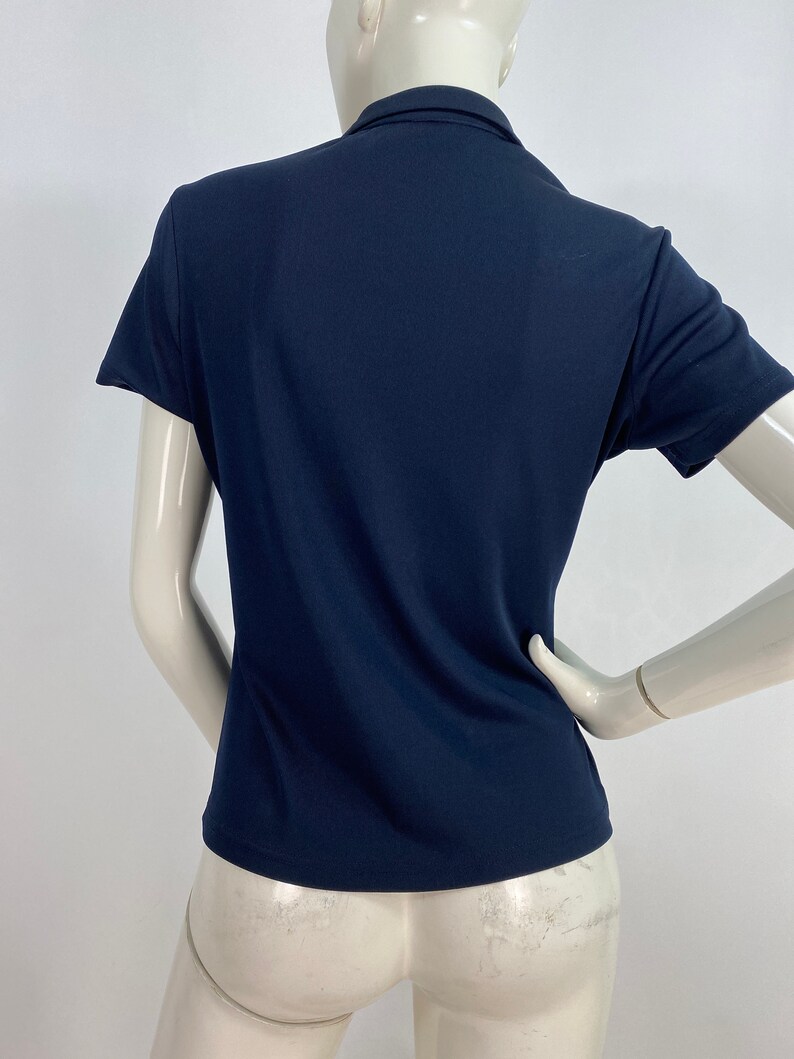 May include: Navy blue short-sleeved collared shirt. The shirt has a classic polo design with a button-up collar and a tailored fit. The fabric appears to be a smooth, solid color.