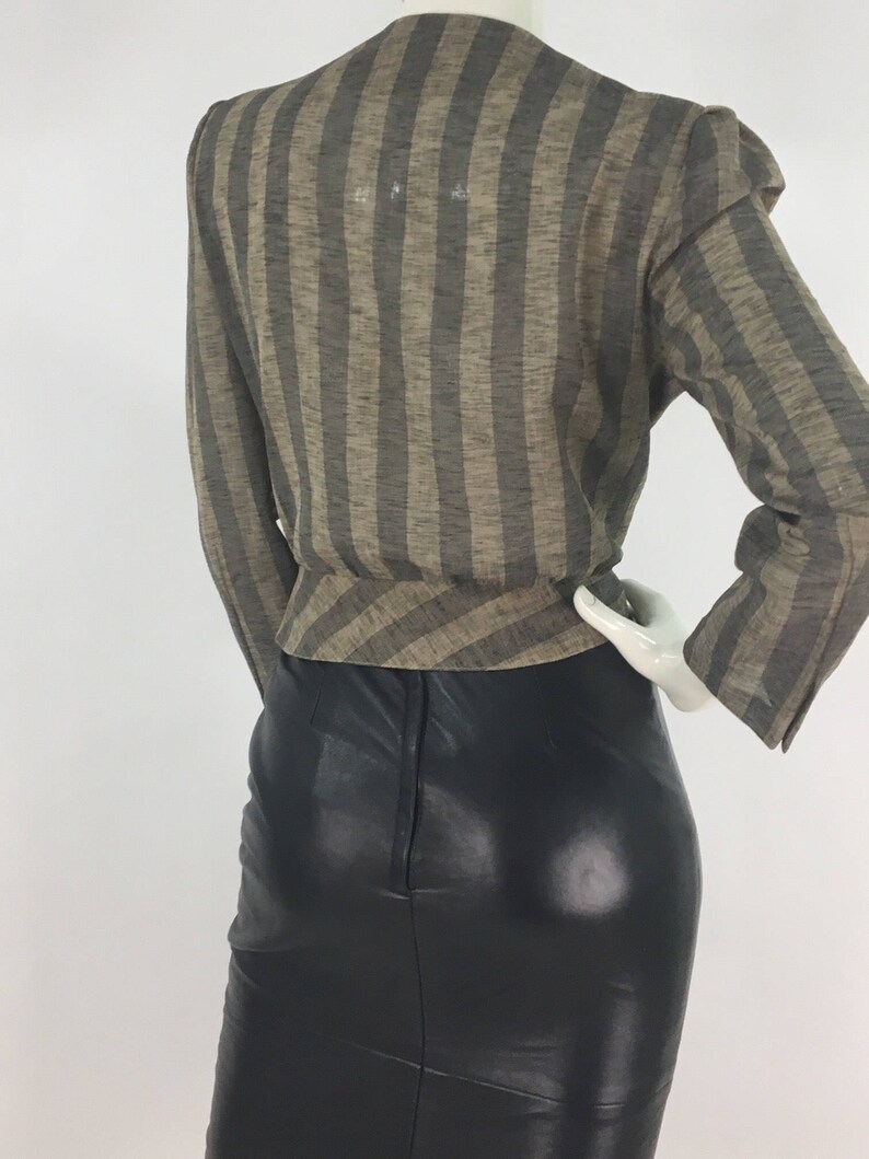 Puede incluir: Una blusa de manga larga con rayas marrones y negras y cuello en V. La blusa se lleva sobre una falda de cuero negra.