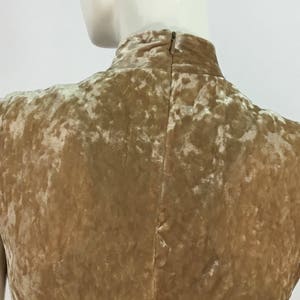 May include: A sleeveless, high-necked dress made of a crushed velvet fabric in a light brown color. The dress has a back zipper closure.