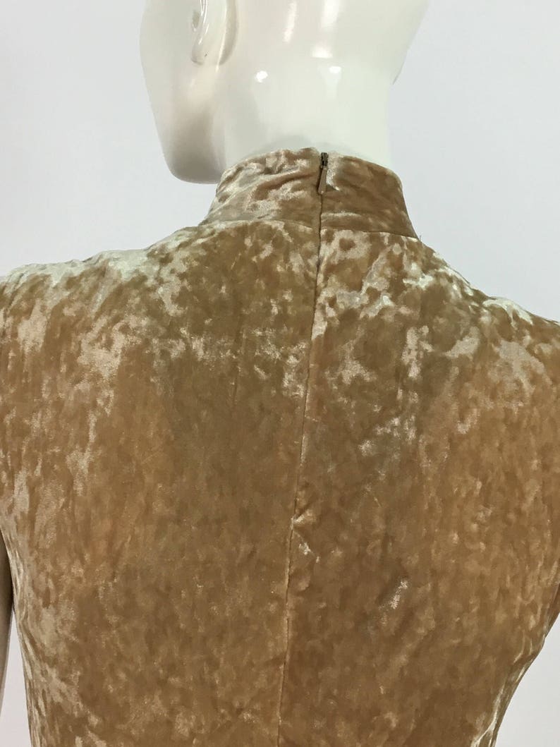 May include: A sleeveless, high-necked dress made of a crushed velvet fabric in a light brown color. The dress has a back zipper closure.