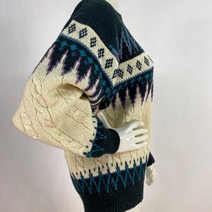 Pode incluir: Um su&eacute;ter de tric&ocirc; com padr&atilde;o creme, preto e azul com detalhes de tric&ocirc; em cabo nas mangas.