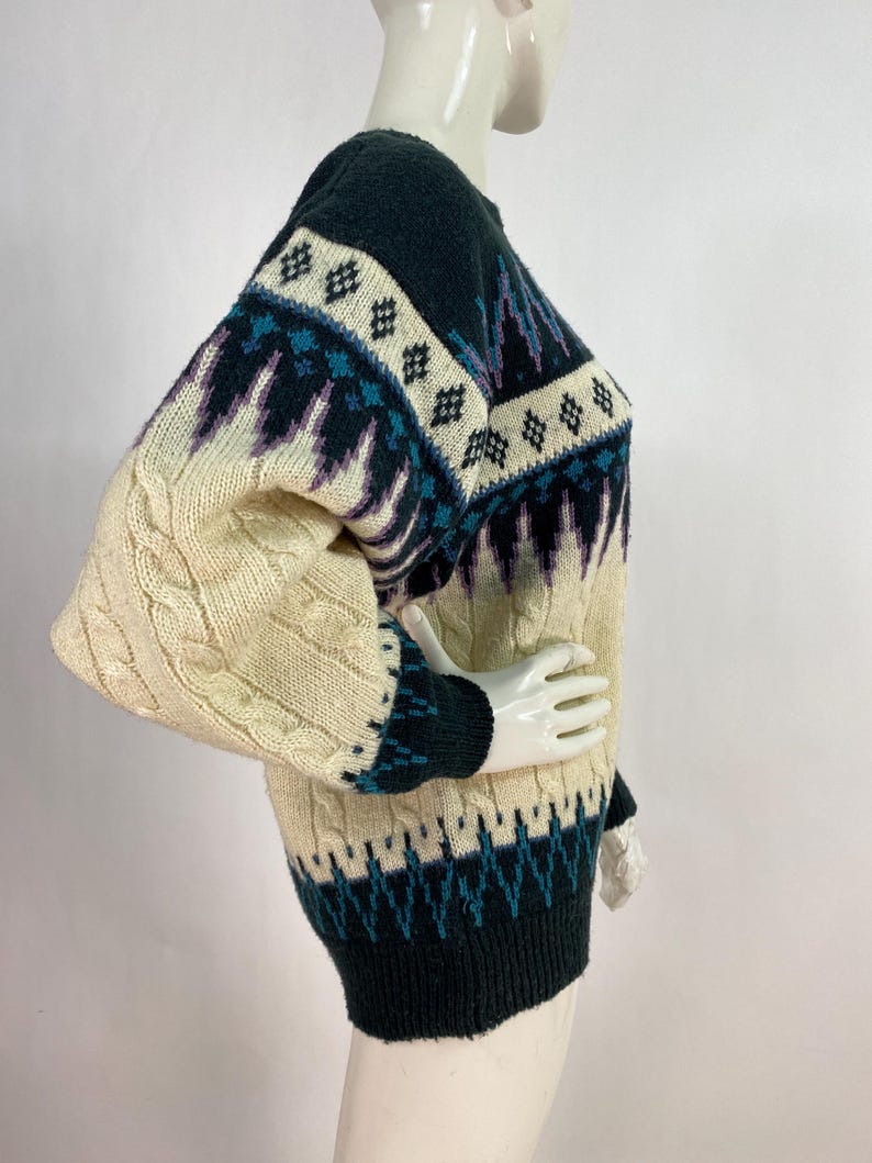 Pode incluir: Um su&eacute;ter de tric&ocirc; com padr&atilde;o creme, preto e azul com detalhes de tric&ocirc; em cabo nas mangas.