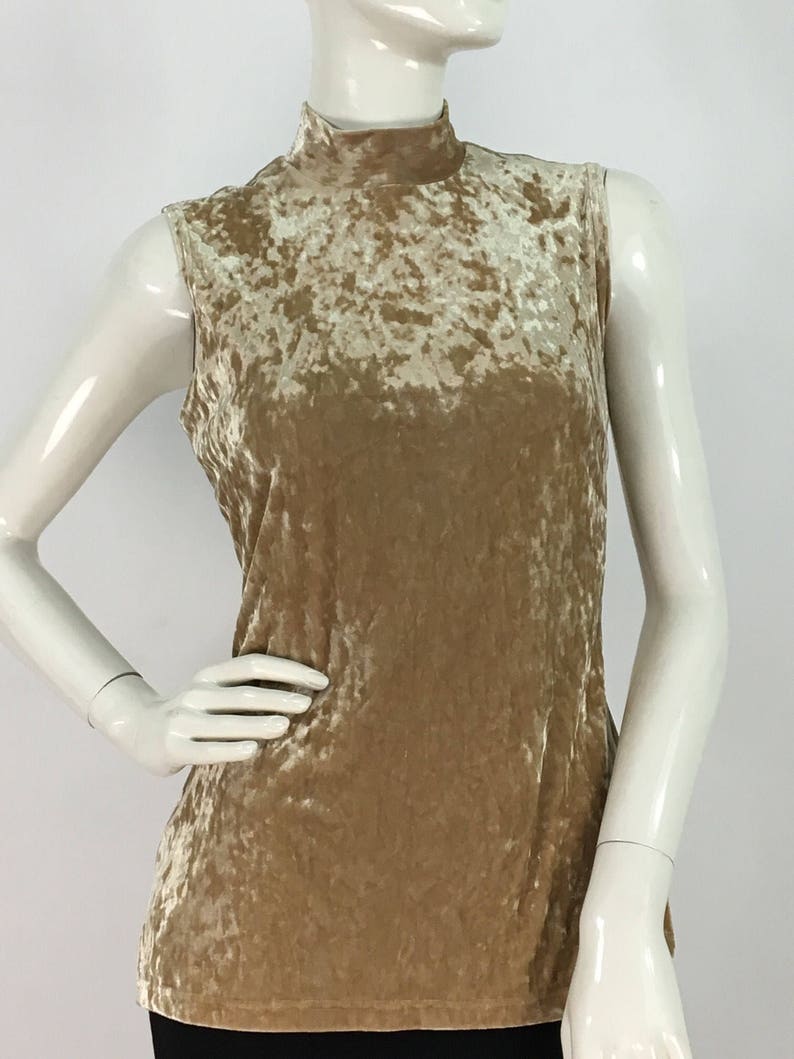May include: A sleeveless, mock neck top made of crushed velvet in a light beige color.