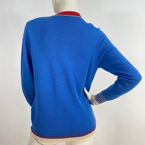 May include: A blue long-sleeved sweater with a red, white, and blue striped trim around the neck and cuffs.