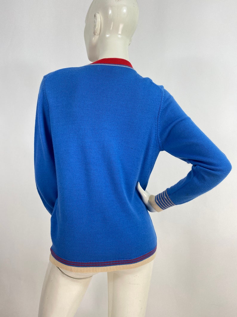 May include: A blue long-sleeved sweater with a red, white, and blue striped trim around the neck and cuffs.