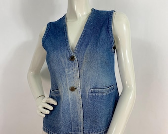 May include: A blue denim vest with a V-neckline and three brown buttons. The vest has two front pockets and a classic, casual style. The vest is sleeveless and appears to be a vintage item.