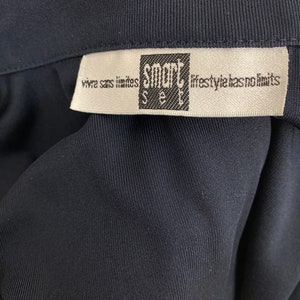 May include: Close-up of a dark navy blue garment with a white label. The label features the text "smart see" in a black square, with the phrases "vivre sans limites" and "lifestyle has no limits" printed on it.