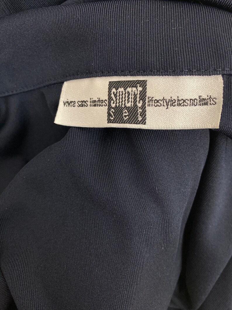 May include: Close-up of a dark navy blue garment with a white label. The label features the text "smart see" in a black square, with the phrases "vivre sans limites" and "lifestyle has no limits" printed on it.