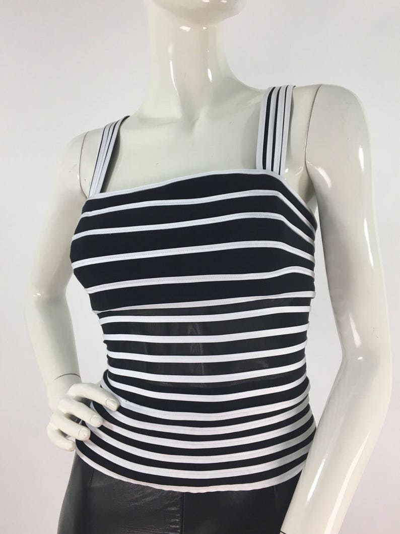 May include: Black and white striped sleeveless top with a square neckline and thin straps. The top is made of a stretchy fabric and has a fitted silhouette.