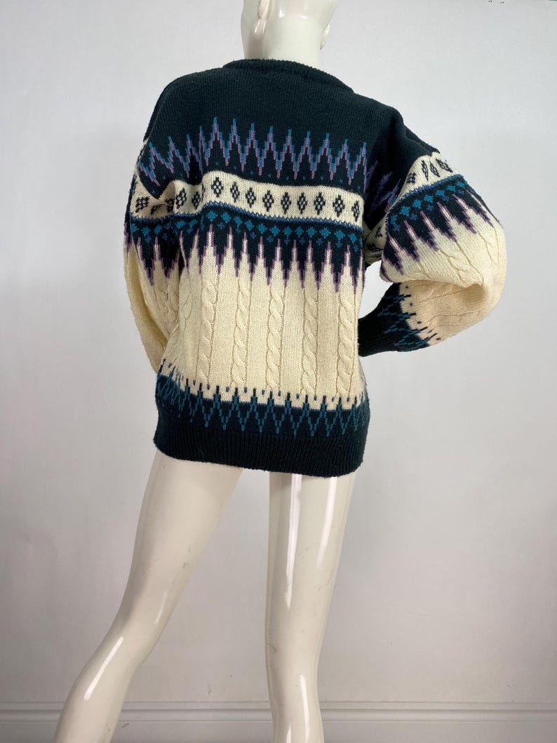 Pode incluir: Um su&eacute;ter de cor creme, verde e roxo com um design de tric&ocirc; de cabo. O su&eacute;ter tem gola redonda e mangas compridas.