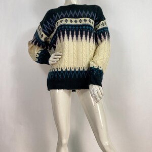 Pode incluir: Um su&eacute;ter preto e creme com um design de tric&ocirc; tran&ccedil;ado. O su&eacute;ter tem gola redonda e mangas compridas.