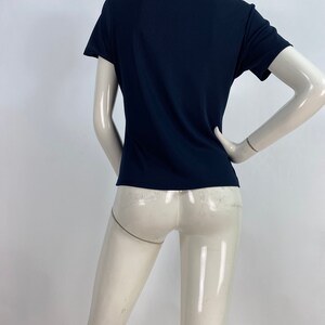 May include: A navy blue short-sleeve polo shirt. The shirt has a classic collar and a fitted silhouette. The fabric appears to be a smooth, knit material. The shirt is displayed on a mannequin.