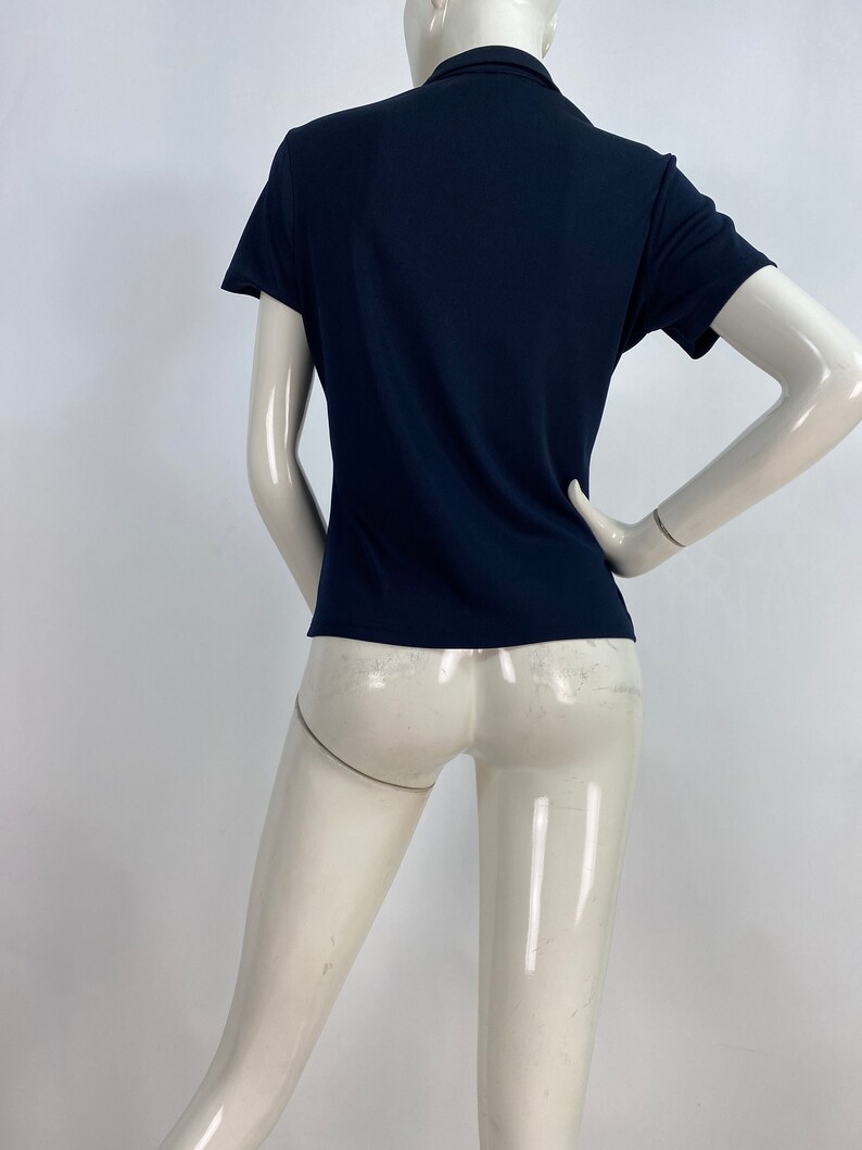 May include: A navy blue short-sleeve polo shirt. The shirt has a classic collar and a fitted silhouette. The fabric appears to be a smooth, knit material. The shirt is displayed on a mannequin.