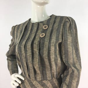 Puede incluir: Una blusa de manga larga a rayas con cintura ajustada y un dobladillo ligeramente acampanado. La blusa tiene un escote redondo y dos botones grandes en la parte delantera.