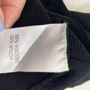 K&ouml;nnte beinhalten: Nahaufnahme eines schwarzen Stofflabels mit wei&szlig;em Text, der "68% Viskose 32% Nylon" lautet.