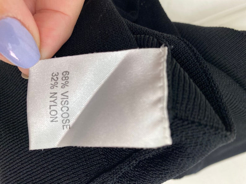 K&ouml;nnte beinhalten: Nahaufnahme eines schwarzen Stofflabels mit wei&szlig;em Text, der "68% Viskose 32% Nylon" lautet.