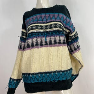 Pode incluir: Um su&eacute;ter vintage multicolorido com um padr&atilde;o geom&eacute;trico preto, branco, azul e roxo. O su&eacute;ter tem gola redonda e mangas compridas.
