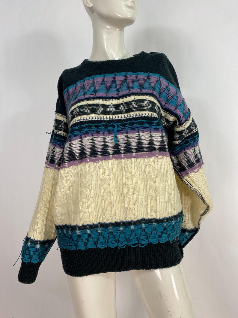 Pode incluir: Um su&eacute;ter vintage multicolorido com um padr&atilde;o geom&eacute;trico preto, branco, azul e roxo. O su&eacute;ter tem gola redonda e mangas compridas.